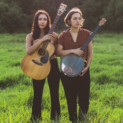 Beide Musikerinnen stehen mit Gitarren in der Hand auf einer Wiese.