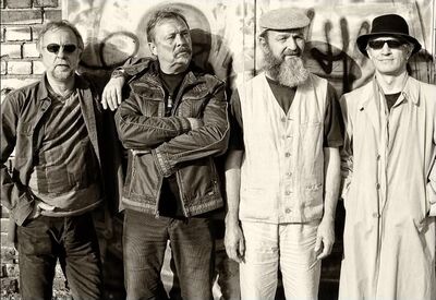 Die vier Musiker der Band stehen nebeneinander an einer Wind, die mit Grafitti besprüht ist.